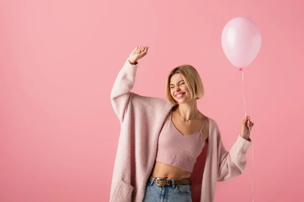 Alegre joven en cárdigan sosteniendo globo aislado en rosa - foto de stock