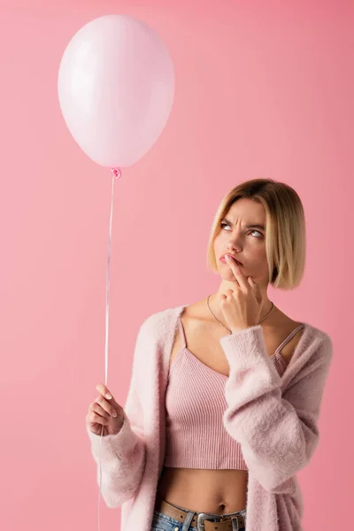 Pensive young woman in cardigan holding balloon isolated on pink — Stock Photo