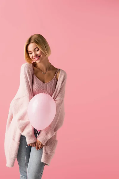 Alegre joven mujer en cárdigan celebración globo aislado en rosa - foto de stock