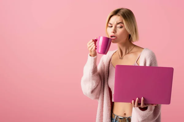 Mulher loira segurando caneca com café e laptop isolado em rosa — Fotografia de Stock