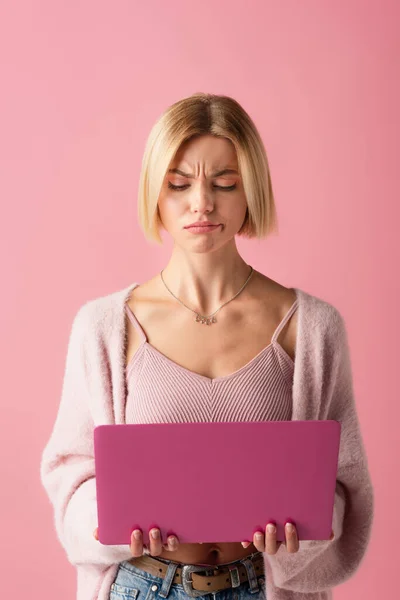 Unzufriedene junge Frau benutzt Laptop isoliert auf rosa — Stockfoto