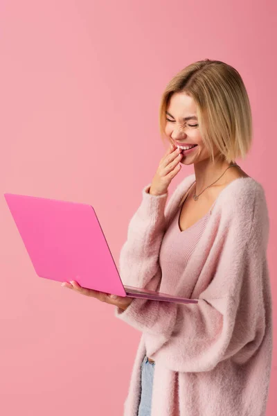 Щаслива молода жінка використовує ноутбук і сміється ізольовано на рожевому — стокове фото