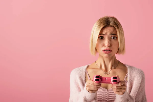 QUIIV, UCRÂNIA - OUTUBRO 29, 2021: mulher chateada segurando joystick e jogando videogame isolado em rosa — Fotografia de Stock