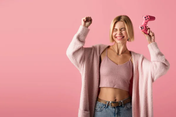KYIV, UCRANIA - 29 de octubre de 2021: una joven excitada sosteniendo un joystick aislado en rosa - foto de stock