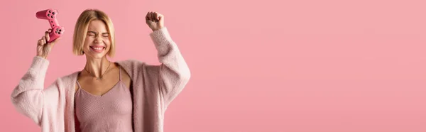 KYIV, UKRAINE - OCTOBER 29, 2021: excited woman holding joystick isolated on pink, banner — Stock Photo