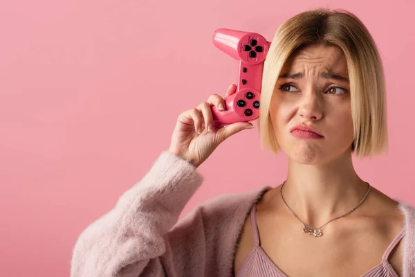 KYIV, UKRAINE - OCTOBER 29, 2021: displeased blonde woman holding joystick isolated on pink — Stock Photo