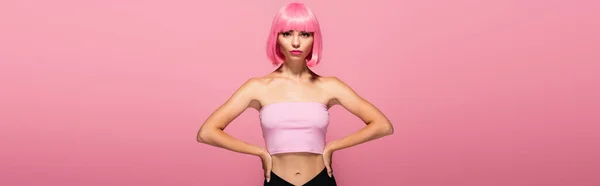 Mujer joven con flequillo y pelo de color posando con las manos en las caderas aisladas en rosa, pancarta - foto de stock