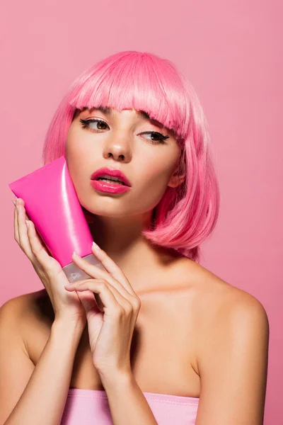 Mujer joven con el pelo de color que sostiene el tubo con la loción aislada en rosa - foto de stock