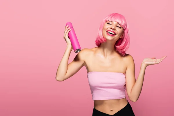 Cheerful woman with colored hair holding bottle with spray isolated on pink — Stock Photo