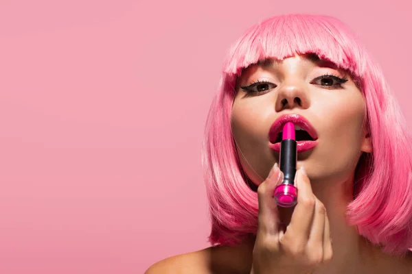 Young woman with colored hair and bare shoulders applying lipstick isolated on pink — Stock Photo