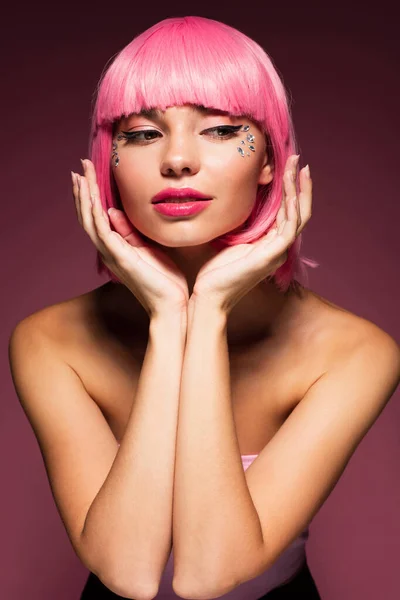 Jolie jeune femme aux cheveux roses et pierres à bijoux brillantes sur le visage sur violet foncé — Photo de stock