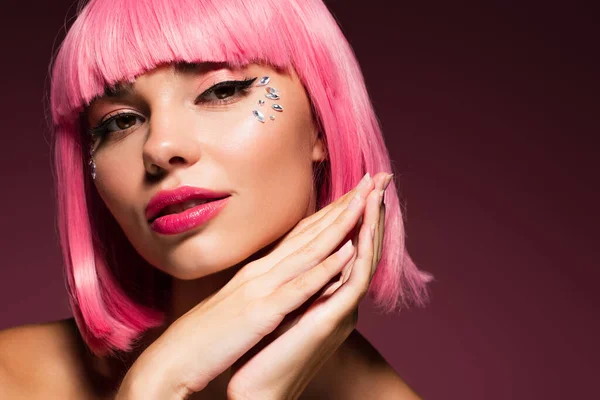 Nahaufnahme einer jungen Frau mit rosa Haaren und glänzenden Schmucksteinen im Gesicht auf dunkelviolett — Stockfoto