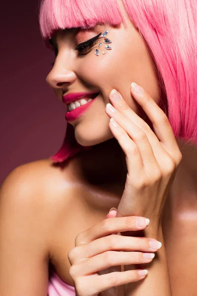 Close up of cheerful woman with pink hair and shiny jewelry stones on face on dark purple — Stock Photo