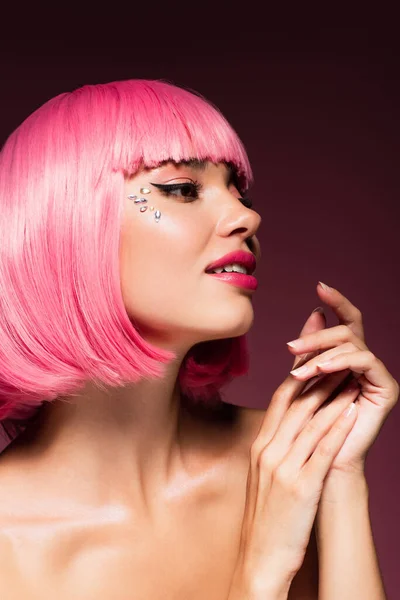 Чуттєва молода жінка з рожевим волоссям і блискучими каменями на обличчі на темно-фіолетовому — стокове фото