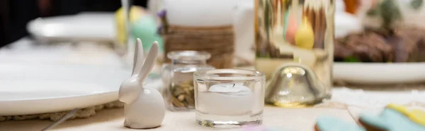 Focus selettivo di coniglio decorativo e candela sul tavolo servito per la cena pasquale, banner — Foto stock