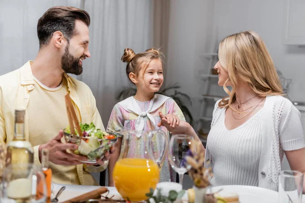 Felice uomo che tiene insalata di verdure vicino moglie e figlia che si tiene per mano durante la cena pasquale — Foto stock