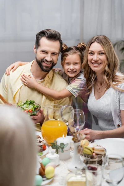 Famiglia felice guardando la fotocamera vicino al tavolo servita con cena pasquale — Foto stock