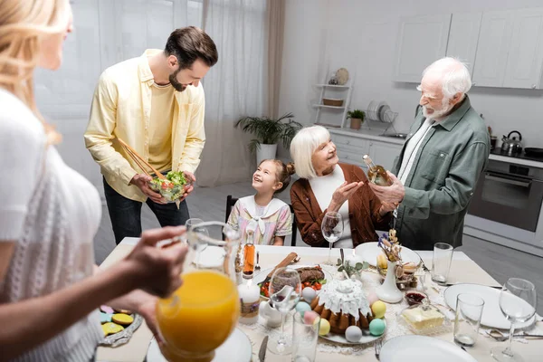 Homens segurando garrafa de vinho e salada de legumes durante o jantar de Páscoa com a família — Fotografia de Stock