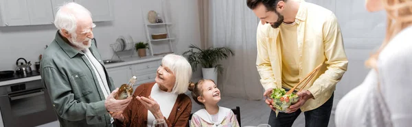 Senior woman pointing with hand near husband holding bottle of wine during easter dinner, banner — Stock Photo