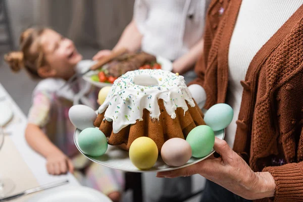 Старша жінка тримає великодній торт біля сім'ї під час святкування Великодня — стокове фото