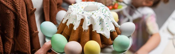 Delicioso pastel de Pascua y huevos pintados cerca de la familia recortada, pancarta - foto de stock