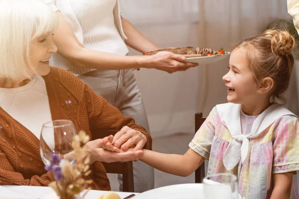 Feliz anciana cogida de la mano de la nieta durante la cena de Pascua con la familia — Stock Photo
