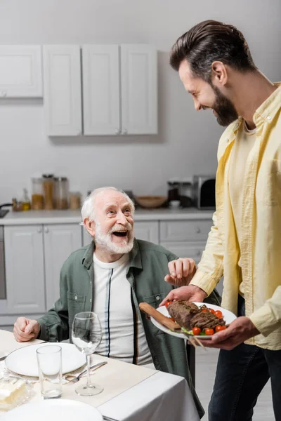 Mann hält Teller mit gebratenem Fleisch beim Osteressen mit lachendem Vater — Stockfoto