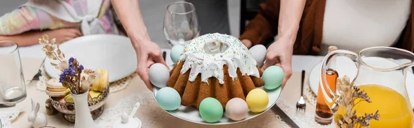 Обрезанный вид на человека, подающего пасхальный торт и окрашенные яйца во время семейного ужина, баннер — стоковое фото