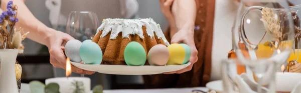 Vista recortada de la mujer sosteniendo plato con sabroso pastel de Pascua y huevos pintados, pancarta - foto de stock