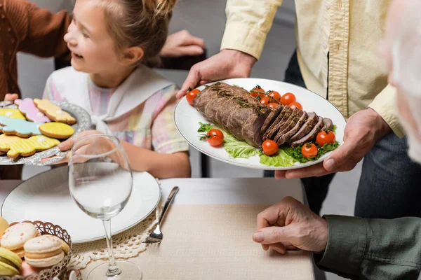 Padre e hija sirviendo galletas tradicionales y carne frita durante la cena de Pascua - foto de stock