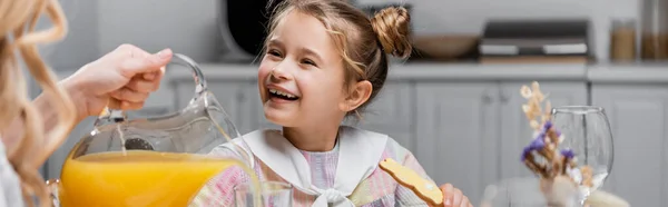 Ragazza sorridente vicino alla madre versando succo d'arancia durante la cena di Pasqua, banner — Foto stock