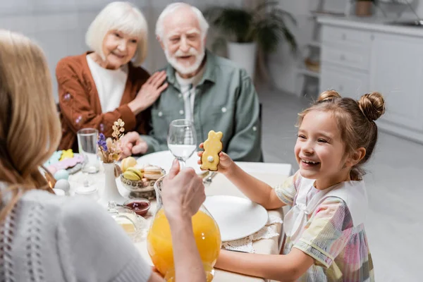 Glückliches Mädchen zeigt Mutter in der Nähe der Großeltern Keks auf verschwommenem Hintergrund — Stockfoto