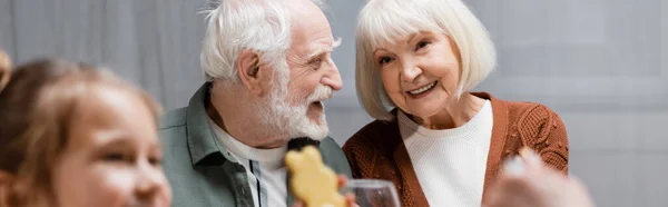 Seniorenpaar lächelt während der Osterfeier neben verschwommenem Mädchen mit Plätzchen, Banner — Stockfoto