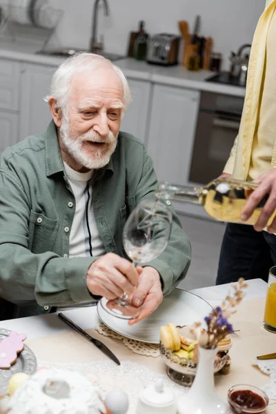 Senior man holding glass near adult son pouring wine during easter dinner — Stock Photo