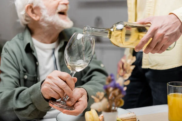 Обрезанный вид человека, наливающего вино в бокал веселого папы на размытом переднем плане — стоковое фото