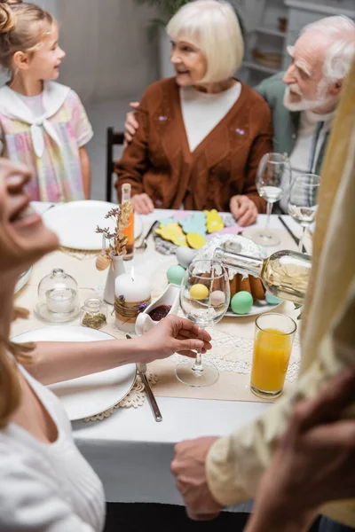 Blurred woman holding glass during easter dinner with family — Stock Photo