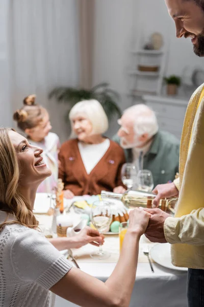 Sonriente mujer cogida de la mano del marido vertiendo vino durante la cena de Pascua - foto de stock