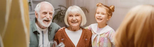 Pareja de ancianos sonriendo cerca de la nieta en primer plano borrosa, bandera - foto de stock