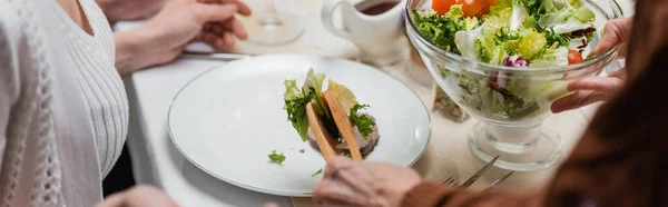 Vista recortada de la mujer mayor con ensalada de verduras y pinzas para servir, pancarta - foto de stock