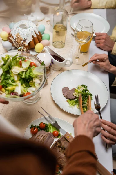 Vista recortada de la familia cerca de ensalada de verduras y pastel de Pascua en la mesa servida - foto de stock