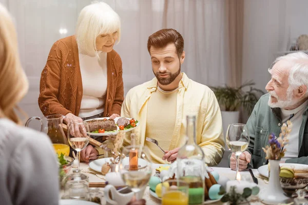 Donna anziana che tiene carne fritta vicino al figlio adulto durante la cena di Pasqua in famiglia — Foto stock