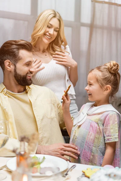 Fille heureuse montrant biscuit de Pâques aux parents heureux — Photo de stock