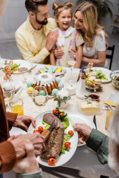 Пожилой человек держит жареное мясо с овощами во время праздничного ужина с семьей — стоковое фото