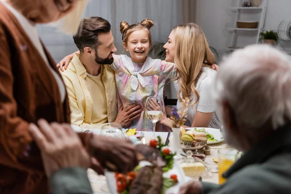 Alegre chica abrazando feliz padres cerca de familia en borrosa primer plano - foto de stock