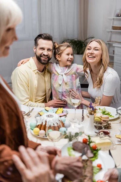 Fille souriant près des parents heureux pendant le dîner de Pâques sur le premier plan flou — Photo de stock