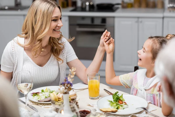 Mãe feliz e filha de mãos dadas enquanto celebra a Páscoa perto do jantar servido — Fotografia de Stock