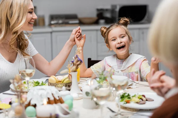 Erstauntes Mädchen hält Hand in Hand mit Mutter und Oma beim festlichen Abendessen auf dem Küchentisch — Stockfoto