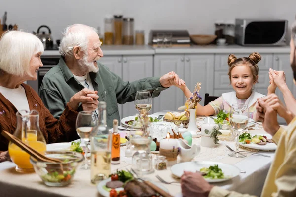 Cheerful family holding hands while sitting at table with easter dinner — Stock Photo