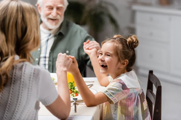 Excitada chica cogida de la mano con borrosa mamá y el abuelo durante la cena de Pascua - foto de stock