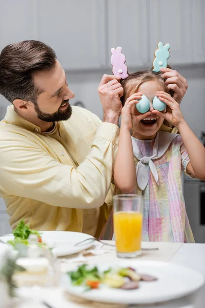 Happy father and daughter having fun with painted eggs and traditional cookies during easter celebration — Stock Photo